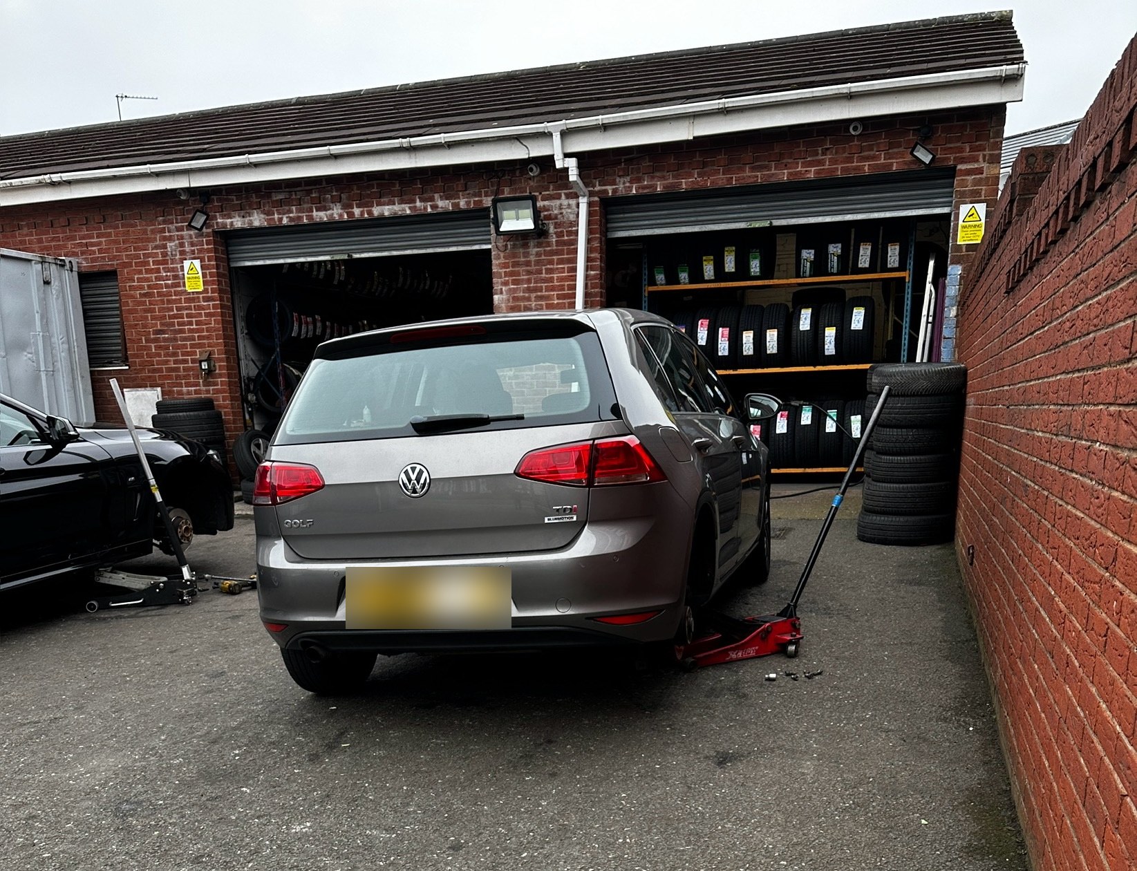 A car on a jack in front of the two fitting bays, with racks of new tyres behind