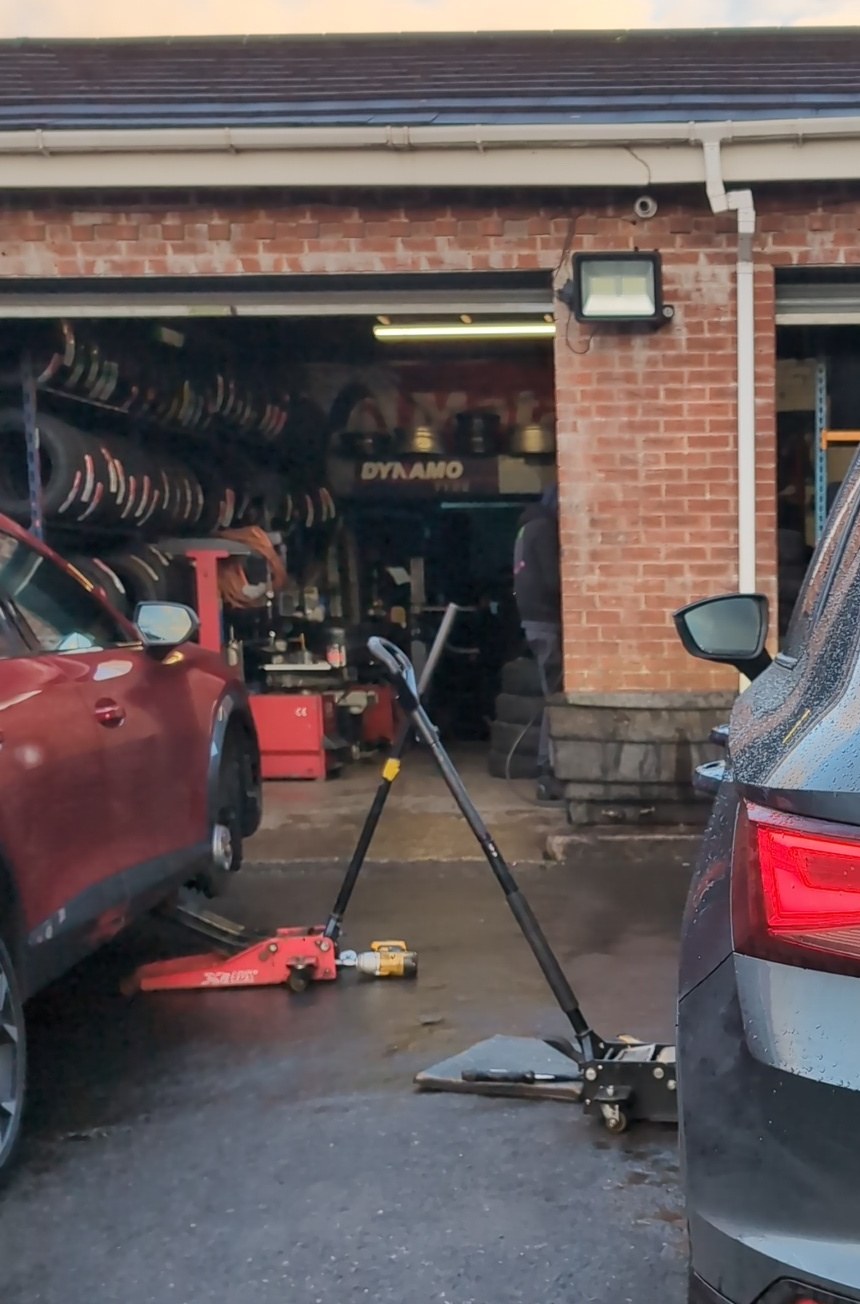 A fitting bay with tyres stacked on racks inside and trolley jacks on the forecourt